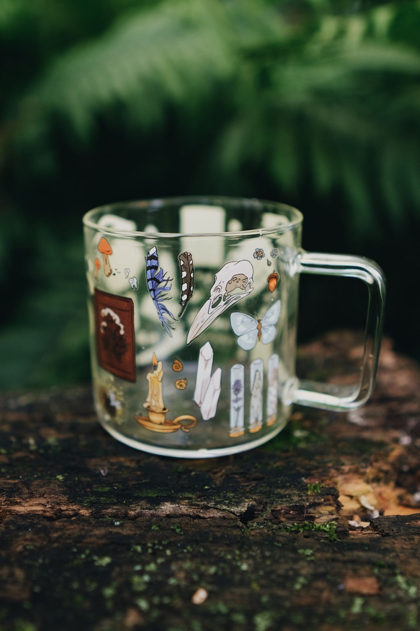 Decorative glass mug with illustrations on a wooden surface with greenery in the background