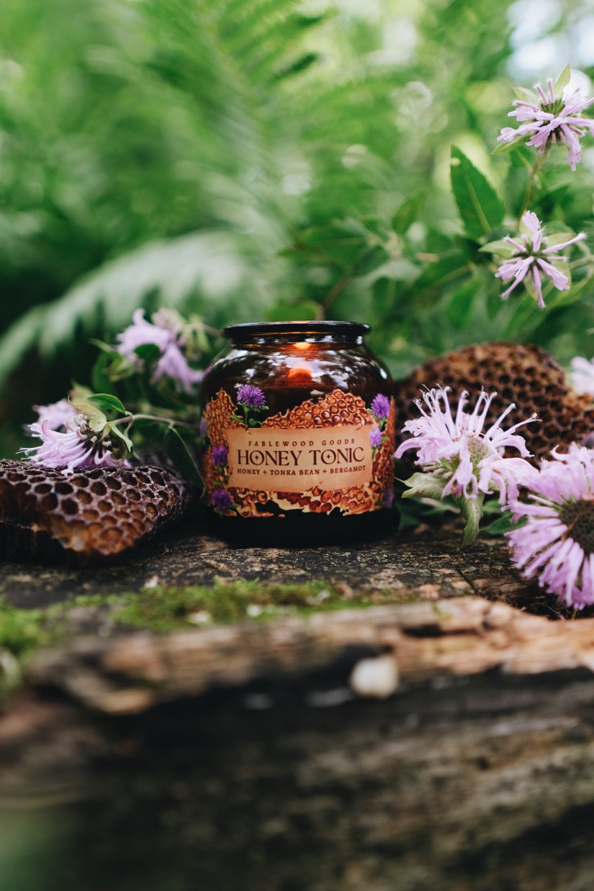 Candle of honey tonic surrounded by flowers and honeycomb on a wooden surface with a natural background