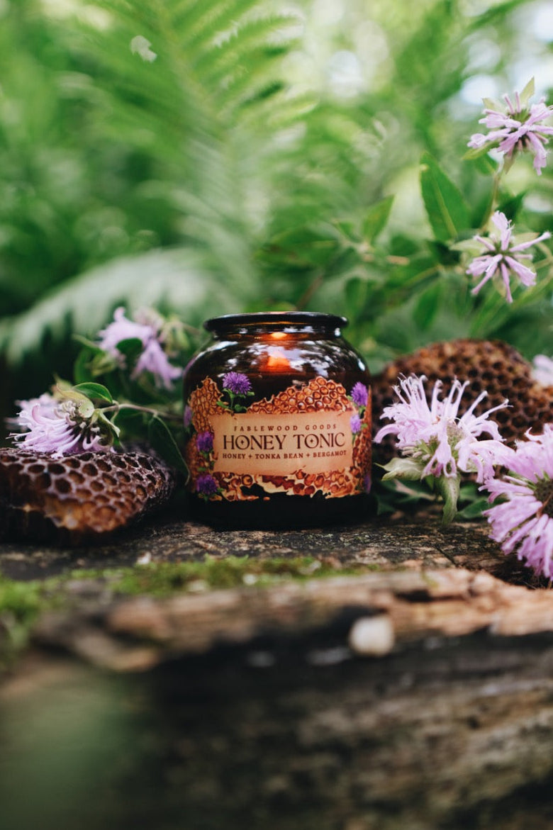Honey tonic candle surrounded by flowers and greenery