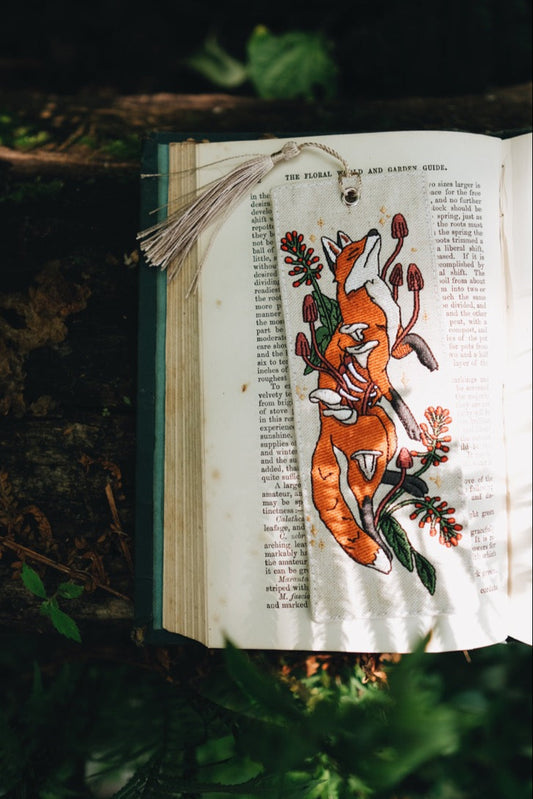 Open book with a fox embroidered bookmark on a leafy background